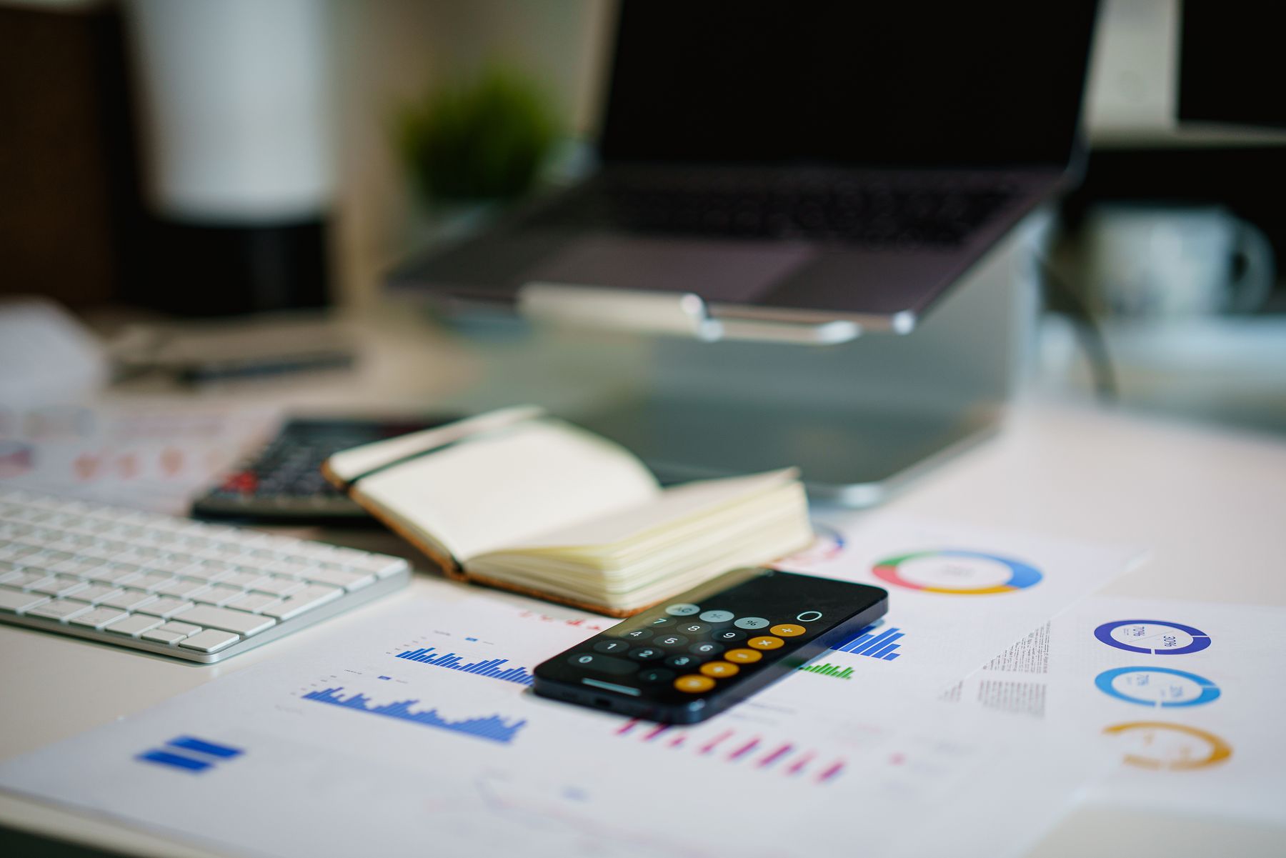 Laptop, calculator, notebook, and performance charts on a worktable
