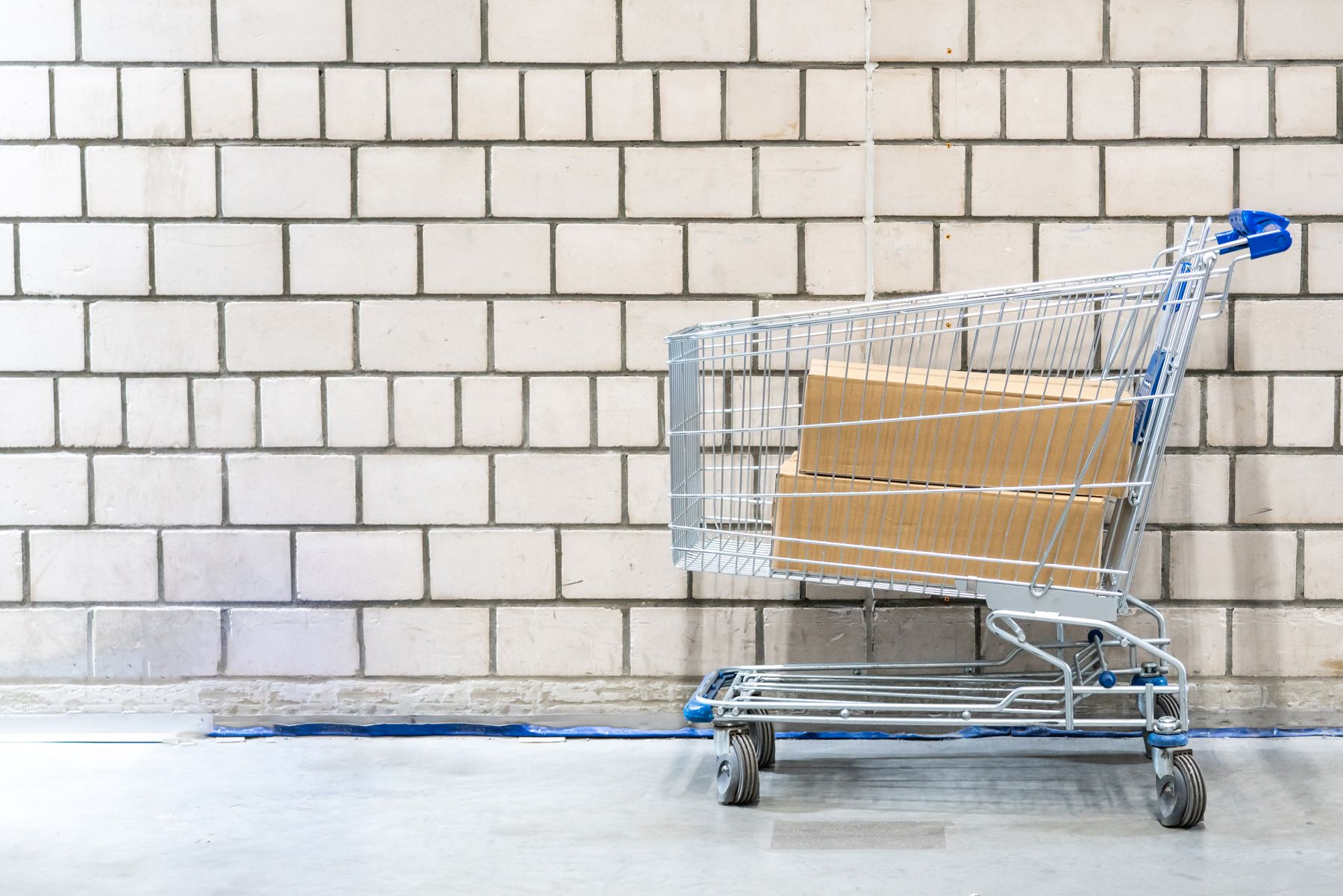 Shopping cart holding shipping boxes against a clean brick wall